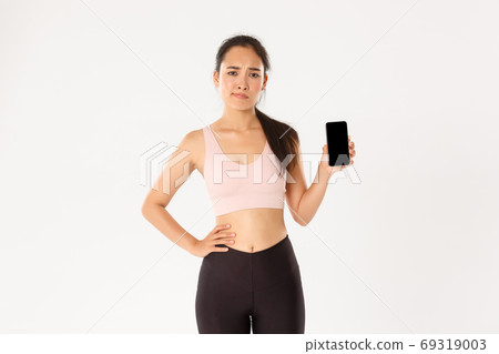 Sport, technology and active lifestyle concept. Dissatisfied and skeptical asian female athlete, sportswoman complaining on fitness application, showing smartphone screen disappointed Sport, technology and active lifestyle concept. Dissatisfied and skeptical asian female athlete, sportswoman complaining on fitness application, showing smartphone screen disappointed 69319003
