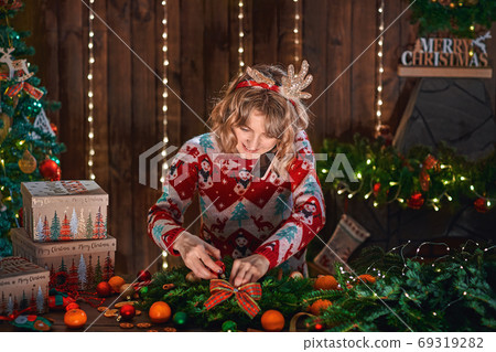 Woman dressed in christmas design sweater making handmade christmas wreath on table for holiday. Christmas decoration and composition Woman dressed in christmas design sweater making handmade christmas wreath on table for holiday. Christmas decoration and composition 69319282