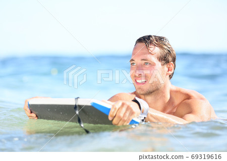 Beach man having fun in water smiling happy. Portrait of young handsome male beach model surfing on bodyboard 69319616