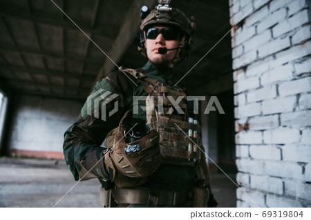 Military man ready to pull a check and to throw a smoke grenade at the building during combat. Military man ready to pull a check and to throw a smoke grenade at the building during combat. 69319804