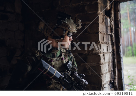 Military man with assault rifle standing inside building, he is ready for combat Military man with assault rifle standing inside building, he is ready for combat 69319811