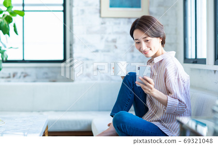 A middle-aged woman watching a smartphone in the living room A middle-aged woman watching a smartphone in the living room 69321048
