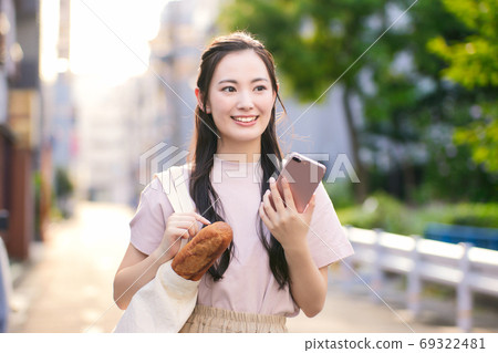 A young woman on the way home from shopping with a smartphone in the city 69322481