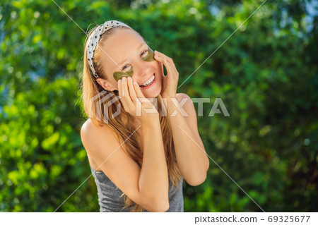 Smiling woman applying hydrogel eye care patches, moisturizing skin under eyes, enjoying skincare procedures 69325677