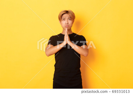 Portrait of miserable asian guy pleading, begging for help, standing over yellow background 69331013