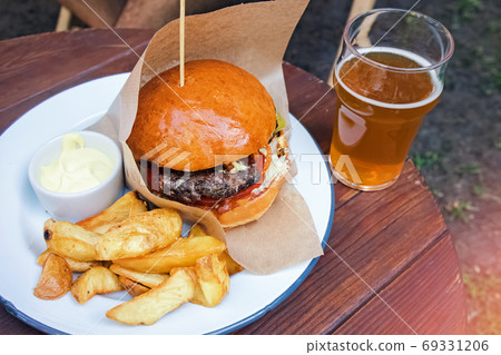 Delicious burger with french fries and a glass on beer on the wooden table Delicious burger with french fries and a glass on beer on the wooden table 69331206