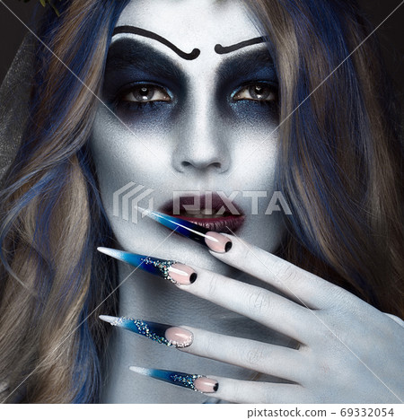 Portrait of a horrible scary Corpse Bride in wreath with dead flowers, halloween makeup and long manicure.Design of nails Portrait of a horrible scary Corpse Bride in wreath with dead flowers, halloween makeup and long manicure.Design of nails 69332054