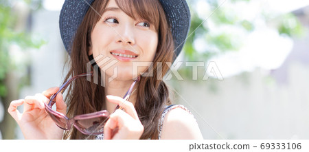 一個微笑與太陽鏡的少婦在她的手上在初夏避暑勝地橫幅大小 一個微笑與太陽鏡的少婦在她的手上在初夏避暑勝地橫幅大小 69333106