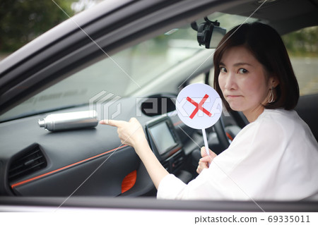 A woman pointing at a spray can and holding a cross tag 69335011