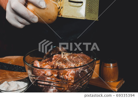 A large piece of pork is cut into pieces, marinated by the chef with spices, and the chef rubs the potatoes on a grater to the marinade. A large piece of pork is cut into pieces, marinated by the chef with spices, and the chef rubs the potatoes on a grater to the marinade. 69335394