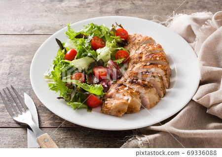 Grilled chicken breast with vegetables on a plate on wooden table. 	 69336088