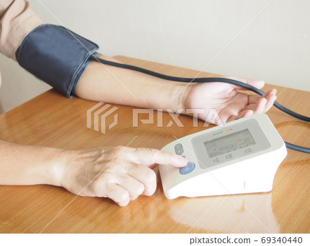 Middle aged women measuring her blood pressure and heart rate with automatic blood pressure monitor at home. Healthcare and medical concept. 69340440