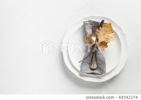 Fall table setting with autumn leaves and white plate 69342174
