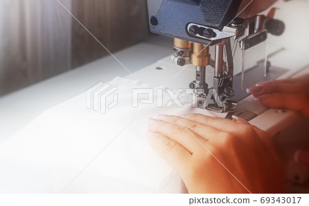 A woman sews on an industrial flat-seam sewing machine. Soft focus A woman sews on an industrial flat-seam sewing machine. Soft focus 69343017