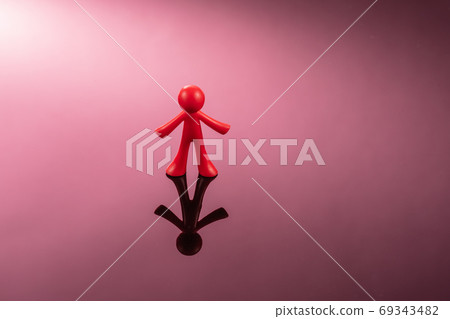 Red plastic figure of a man standing on a mirror pink surface Red plastic figure of a man standing on a mirror pink surface 69343482
