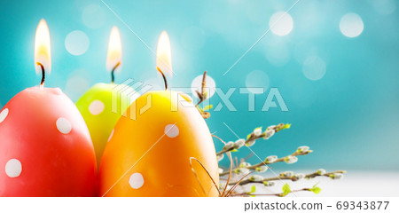 Easter colorful candle eggs with willow twigs on blurred blue background with bokeh lights. Copy space. Soft focus 69343877