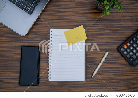 Striped brown working table with note pad, mobile phone, pen, calculator a laptop and table plant on display. 69345569