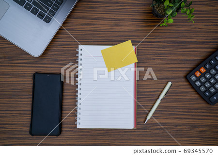 Striped brown working table with note pad, mobile phone, pen, calculator a laptop and table plant on display. 69345570