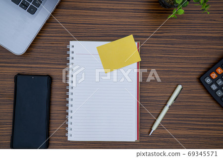 Striped brown working table with note pad, mobile phone, pen, calculator a laptop and table plant on display. 69345571