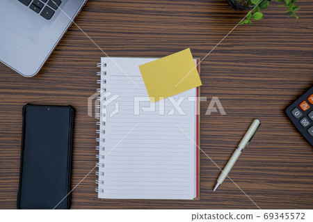 Striped brown working table with note pad, mobile phone, pen, calculator a laptop and table plant on display. 69345572