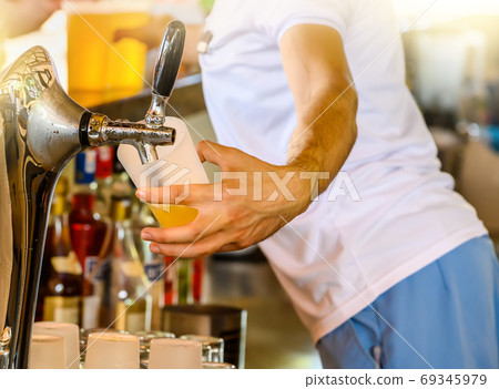 Bartender pours the beer into a glass from the tap. Selective focus on tap. Bartender pours the beer into a glass from the tap. Selective focus on tap. 69345979