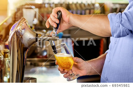 Barman pours the beer into a glass from the tap. 69345981