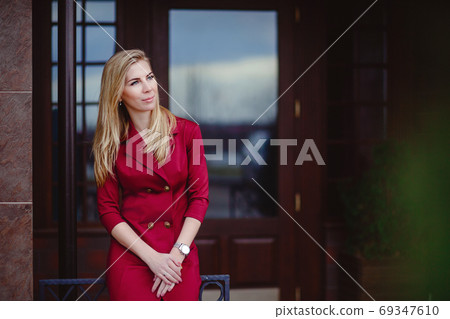 Young beautiful blonde in a red dress in the city. A business woman goes to work. Female businessman. Young beautiful blonde in a red dress in the city. A business woman goes to work. Female businessman. 69347610