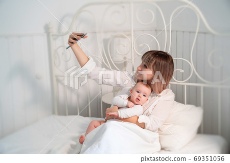 mom with baby in bed taking selfies  69351056