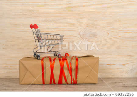 craft paper wrapped gift with red ribbon and shopping trolley 69352256