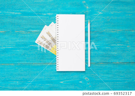 empty notepad with white pencil and 200 euro banknotes on turquoise wooden table, copy space 69352317