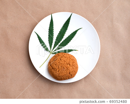 Cannabis leaf with cookies on a white plate. Cannabis live resin extraction on kraft background. Cannabis leaf with cookies on a white plate. Cannabis live resin extraction on kraft background. 69352480