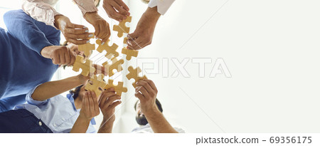 Happy company employees joining parts of jigsaw puzzle during work meeting or team building activity Happy company employees joining parts of jigsaw puzzle during work meeting or team building activity 69356175