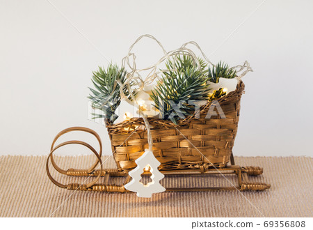 Christmas decoration on the table. Santas sleigh with twigs and lights in the shape of fir trees. 69356808