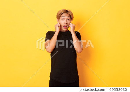 Excited handsome blond guy in black clothes, looking tempted and standing over yellow background Excited handsome blond guy in black clothes, looking tempted and standing over yellow background 69358080