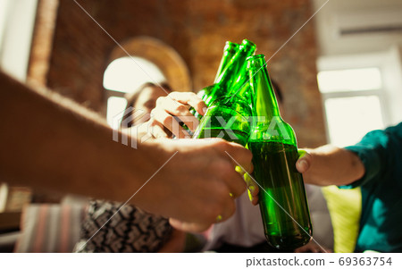 Young group of friends drinking beer, having fun, laughting and celebrating together. Close up clinking beer bottles Young group of friends drinking beer, having fun, laughting and celebrating together. Close up clinking beer bottles 69363754
