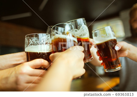 Young group of friends drinking beer, having fun, laughting and celebrating together. Close up clinking beer glasses Young group of friends drinking beer, having fun, laughting and celebrating together. Close up clinking beer glasses 69363813