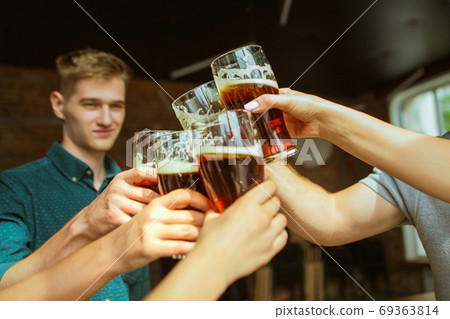 Young group of friends drinking beer, having fun, laughting and celebrating together. Close up clinking beer glasses Young group of friends drinking beer, having fun, laughting and celebrating together. Close up clinking beer glasses 69363814