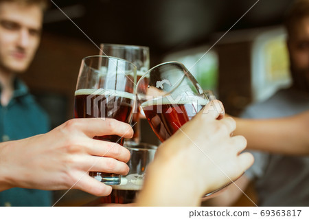 Young group of friends drinking beer, having fun, laughting and celebrating together. Close up clinking beer glasses 69363817