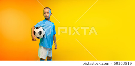 Young boy as a soccer or football player in sportwear practicing on gradient yellow studio background in neon light Young boy as a soccer or football player in sportwear practicing on gradient yellow studio background in neon light 69363819