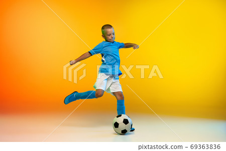 Young boy as a soccer or football player in sportwear practicing on gradient yellow studio background in neon light 69363836