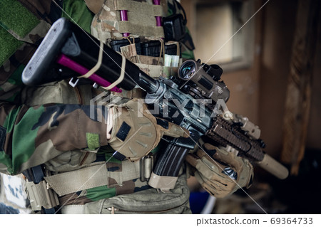 Weapons close-up on a military man standing inside the building and waiting for command. Weapons close-up on a military man standing inside the building and waiting for command. 69364733