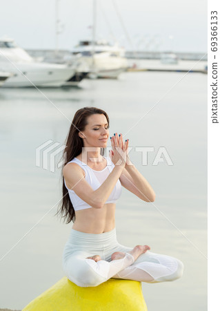 Young sportive woman is sitting on sea, marina pier and looking at horizon 69366133