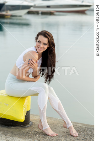 Young sportive woman is sitting on sea, marina pier and looking at horizon 69366154