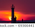 sun rising behind lighthouse along with fisherman 69366441