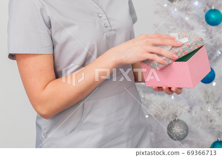 Woman smiling in medical uniform with gift box Woman smiling in medical uniform with gift box 69366713
