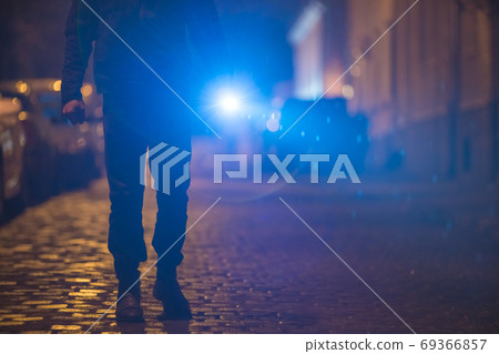 The man with a bright flashlight stand on the street. Evening night time 69366857