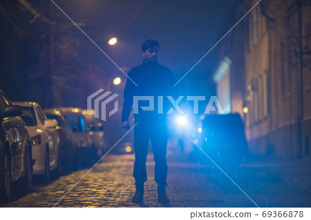 The man with a flashlight stand on the street. Evening night time 69366878