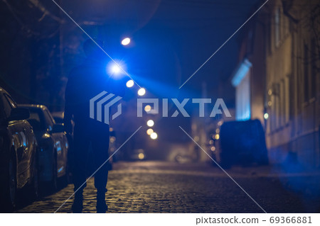 The man with a flashlight stand on the street. Evening night time 69366881