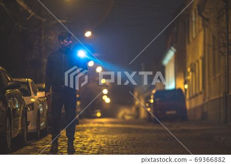 The man with a flashlight stand on the street. Evening night time 69366882