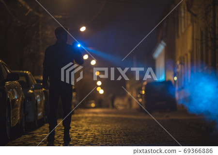 The man with a flashlight stand on the road. Evening night time The man with a flashlight stand on the road. Evening night time 69366886